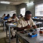 Create an editorial news illustration for an article about 'Prison de Brazzaville : les détenus veulent des examens techniques pour une réinsertion réussie'. The specific country is Republique du Congo (Brazzaville) (CG); make visual cues accurate to